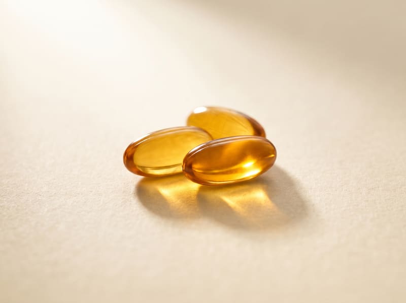 Three translucent golden oil capsules, backlit so the oil inside glows.