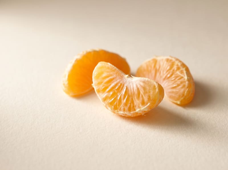 Three fresh orange citrus segments on a warm cream surface.
