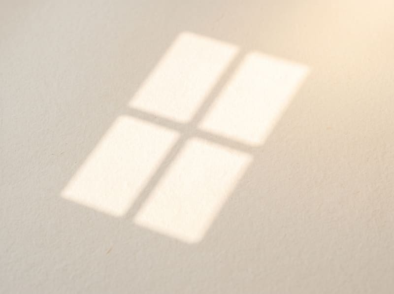 A shaft of daylight falling across a cream surface, casting the soft shadow of a window frame.
