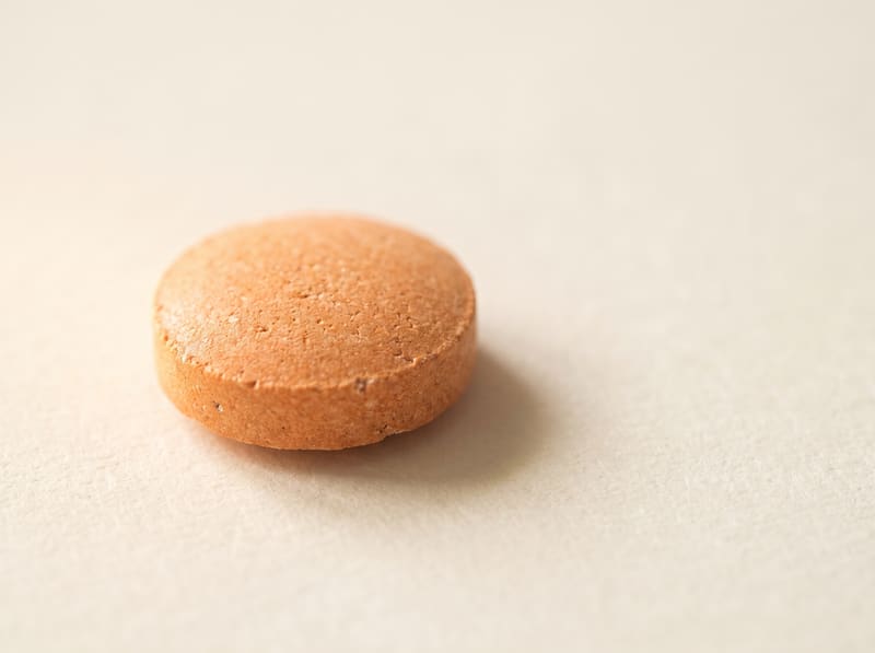 A single matte orange chewable tablet, its milled surface texture visible in raking light.
