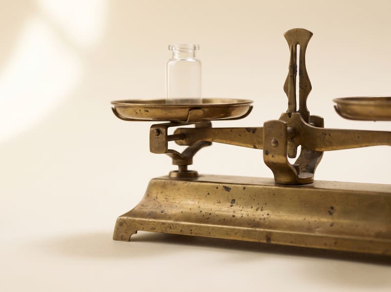 A vintage brass apothecary balance scale beside a plain glass bottle.